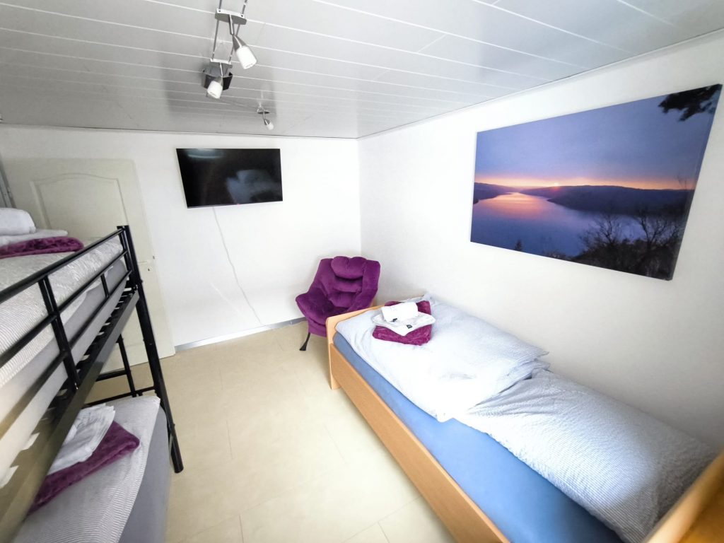 Zweites Schlafzimmer im Ferienhaus CaSa Hürtgenwald mit Etagenbett, Einzelbett und modernem Smart-TV.