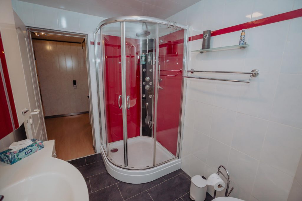 Modernes Badezimmer im Ferienhaus CaSa Hürtgenwald mit Glasduschkabine und roten Akzenten.