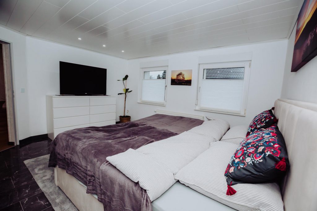 Modernes Schlafzimmer mit großem Doppelbett, dunklem Marmorboden und TV-Ecke.