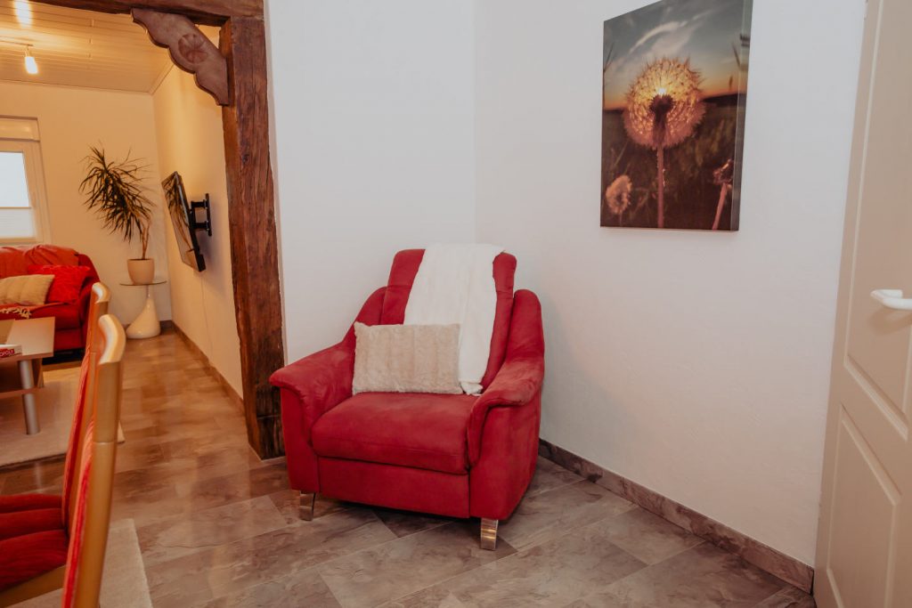 Gemütliche Leseecke mit rotem Sessel und Wandbild im Ferienhaus CaSa Hürtgenwald